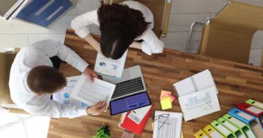 Ofis çalışanları, şirket projesini ahşap masadaki çizelgelerle dizüstü bilgisayara bakarak tartışıyor. Erkek ve kadının üst görüşü iş toplantısı