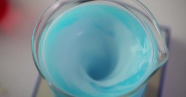 Laboratuvar çalışanları tarafından profesyonel kullanım için kullanılan cam şişede dönen mavi sıvı. Deney süreci ve ekipman yavaş çekim