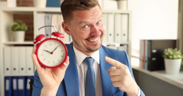 午前10時の赤い目覚まし時計を持つ笑顔のマネージャーの肖像画 勤務日の概念の開始 — ストック動画