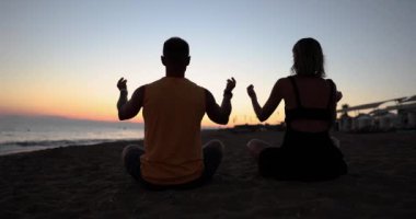 Two meditating at sunset sitting on the beach, back view. Yoga pose, relaxation on vacation, golden hour