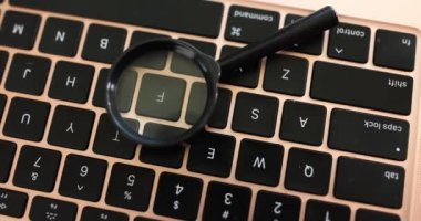 The magnifying glass lies on a computer keyboard, close-up, elevated view. Theft of personal data, hacking