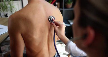 Doktor steteskopu bir adamın sırtına bastırıyor, yakın plan. Doktoru ziyaret et, grip teşhisi koy.