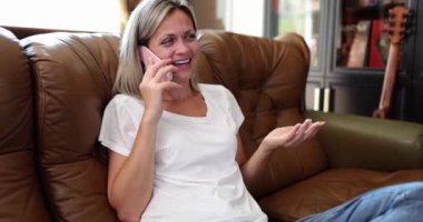 A happy woman at home on the couch speaks on a smartphone, close-up. Communication, positive emotions