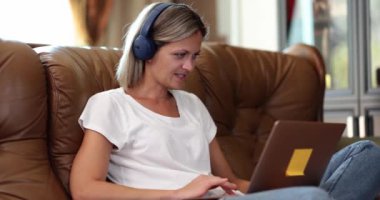 A woman in headphones on the couch uses a laptop, close-up. Distant work, enjoying leisure time with gadget