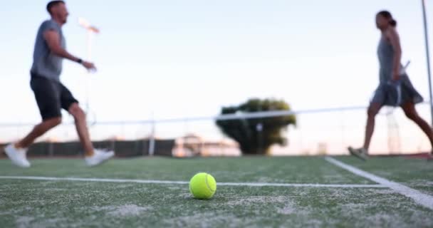 Желтый Теннисный Мяч Лежит Зеленой Площадке Поверхностный Фокус Радостные Игроки — стоковое видео