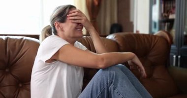 A young woman cries at home on a leather sofa, a close-up, slowmotion. Concepts loss, resentment shallow focus