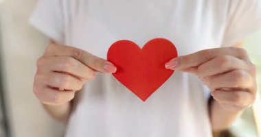 Young female hands hold a red paper heart, a close-up. Concept recognition of love, affection and friendship
