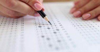Macro female hands mark educational test options with a pencil, slowmotion. Multiple choice question, close-up