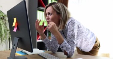 A young woman in the office at a computer monitor grabs her head, close-up. Business error, problematic at work
