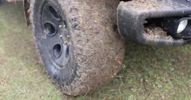 Close-up car with a dirty wheel on the grass, slowmotion. Road without asphalt, the front of the SUV in the swamp