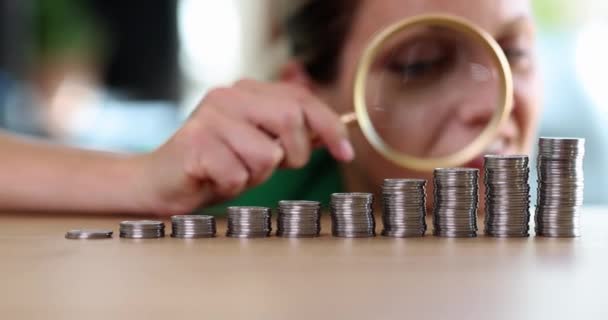 一个女人拿着放大镜看了看桌子上一排硬币 投资增长 — 图库视频影像