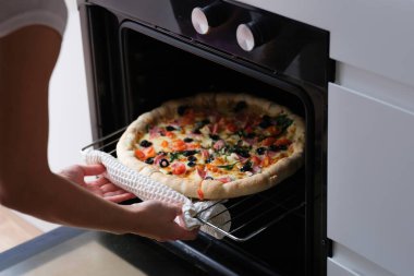 Kadın pizza tepsisini fırına koyuyor. Ev konseptinde pizza pişirmek