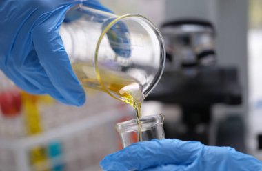 Kimyasal laboratuvar araştırması ve sıvı yağ işleme. Bilim adamı, kimyasal test tüpünden cam şişe konseptine elle sarı sıvı döküyor.