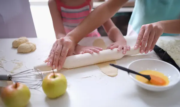 Mom and daughter roll out the dough with rolling pin in kitchen. Family cooking pastry concept