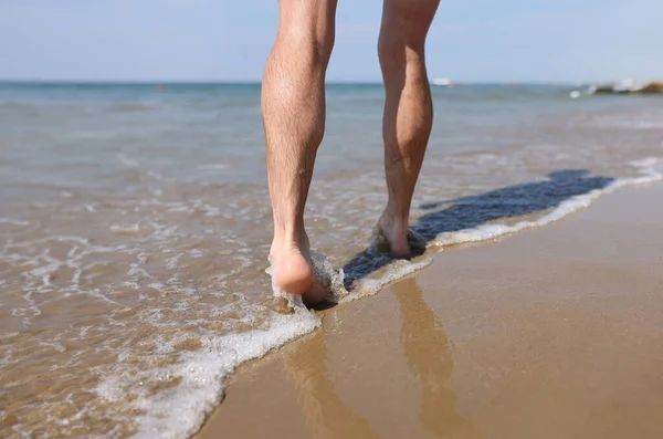 Man feet walking along sandy beach closeup. Summer vacations concept