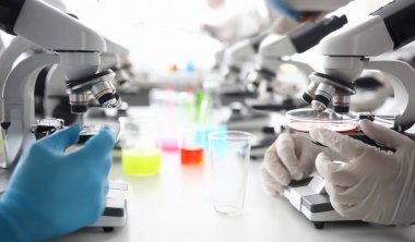 Koruyucu lateks eldivenlerde erkek eli. Adli tıp laboratuarında birçok mikroskop closeup backgroung. Özel ekipman ve kimyasal madde satışı konsepti