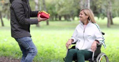 Park 4K filminde tekerlekli sandalyedeki engelli kadına hediye veren genç bir adam. Engelli insanlarla yakın ilişkiler
