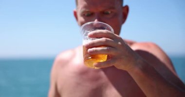 Yazın kumsalda duygusal açgözlülükle soğuk bira içen bir adam. Yaz sıcağında taze biranın tadını çıkar.