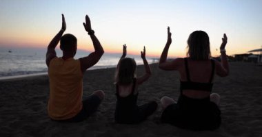 Aile plajda yoga yapıyor ve yaz tatilinde seyahat ediyor. Dinlenme ve aile uyumu.