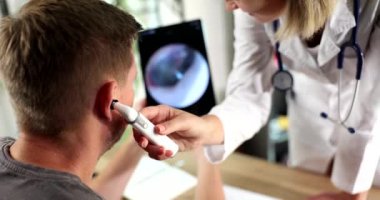 Duyma kliniğinde kulak muayenesi sırasında yetişkin bir erkek. Odiyolog, ekranda görüntüsü olan dijital otoskoplu erkek hastanın kulağını inceliyor.