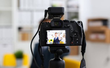 Erkek takım elbise ve kravat göstermek onaylamak işareti kol yapma promo videoblog veya fotoğraf oturumunda office video kamera tripod taşımak için. Vlogger tanıtım selfie çözüm ya da Finans Danışmanı yönetimi bilgileri