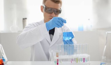 Erkek bir kimyager elinde cam test tüpü tutarak potasyum permanganatın sıvı çözeltisini taşır. Kimyasal imalatı kullanarak çeşitli reaksiyonlar uygular.