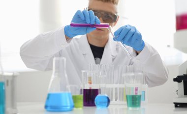 Erkek bir kimyager elinde cam test tüpü tutarak potasyum permanganatın sıvı çözeltisini taşır. Kimyasal imalatı kullanarak çeşitli reaksiyonlar uygular.