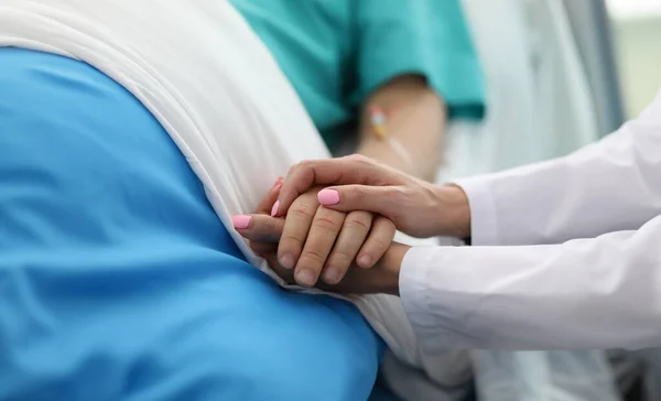 Close-up of people holding hands of each other. Woman calming to sick patient in hospital ward. Doc asking about well-being of sick person. Healthcare and medicine concept