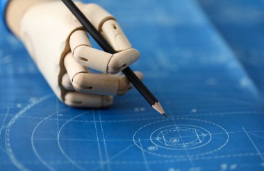 İnsan elinin protezle yakın çekimi masanın üzerinde planlarla çalışıyor. Kalem tutan ahşap kollu biri. İş ve engelliler konsepti