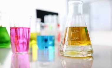 Laboratuvar masasında parlak sarı, pembe ve mavi sıvı bulunan saydam cam tıbbi şişelerin yakın çekimi. Üç tüp analiz altında. Tıp ve araştırma kavramı