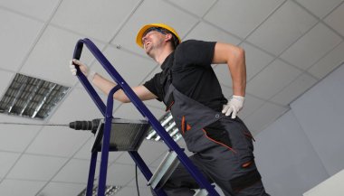 Sırt ağrısından bağıran bir uzman. Tornavidayla metal merdivenin üzerinde duran kötü sağlık sorunu olan profesyonel bir tamirci. Teknisyenlerin omurga ağrıları