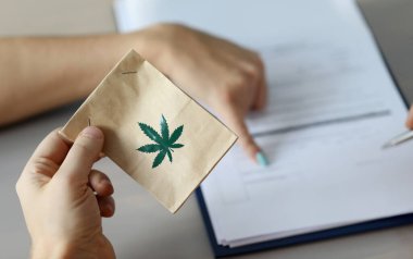 Üzerinde esrar işareti olan erkek eli verme paketine odaklan. Doktor tedavi randevuları yazıyor ve hasta için tabela gösteriyor. Sağlık ve tıbbi marihuana konsepti