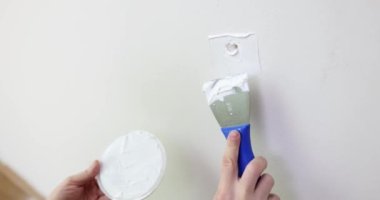 Çatlak beyaz duvarı spatulayla tamir eden bir adam. Duvarların ve açıkların onarımı