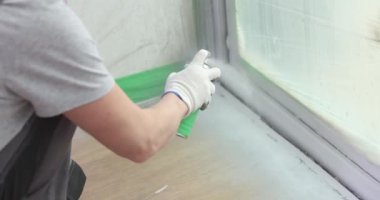 İnşaatçı beyaz sprey boyayla bir pencere katmanı boyuyor. Boya kapısı ve pencere yamaçları