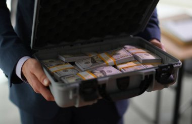 Banker holding suitcase with many dollar bills closeup. Crime and fraud giving bribe on large scale concept clipart