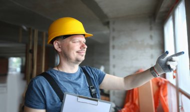 Miğferli erkek müteahhit inşaat alanına pencereden bakıyor. Foreman ustabaşı ve inşaat projelerinin ustabaşı.