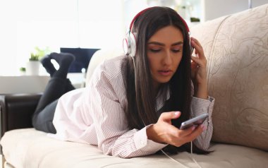 Kulaklıklı genç bir kadın kanepede dinleniyor ve internet üzerinden akıllı telefon kullanarak müzik dinliyor. Telefon için müzik ve eğitim uygulamaları