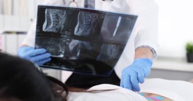 Osteopat, Kinesio bantlı hastanın belkemiğini elliyor ve omurga filmi ağır çekimde röntgene bakıyor. Travma sonrası rehabilitasyon kinezi konsepti