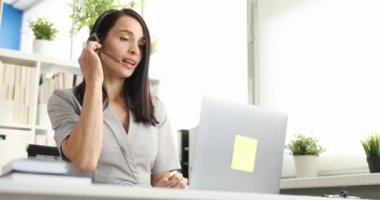 Kulaklık ve mikrofonlu bir kadın dizüstü bilgisayar ekranı 4K film yavaş çekim ile iletişim kuruyor. Çağrı merkezi konseptinde operatör olarak çalış