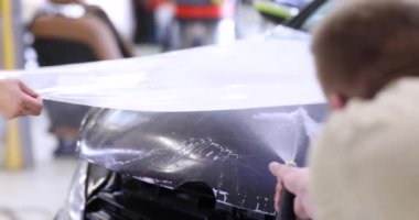 Arabanın kaputunu koruyucu plastik film 4K ağır çekimle kaplayan usta bir tamirci. Araba temizleme servisi kavramı