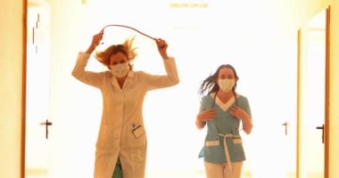 Koruyucu maskeli kadın doktorlar kliniğin koridorunda ağır çekimde koşuyorlar. Acil tıbbi bakım konsepti