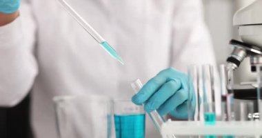 Pipetten alınan eldivenlerle bilim adamı laboratuardaki test tüpüne mavi sıvı damlatıyor. Sıvı kimyasal araştırma konsepti