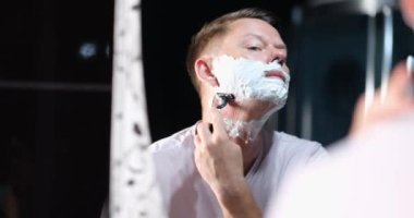 Handsome man with white foam shaves hair. Male stubble and facial skin care concept