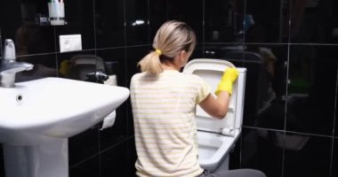 Eller evdeki tuvalet kağıdıyla klozet kapağını temizliyor. Sarı lastik eldivenli kadın tesisat konseptini temizler ve yıkar.