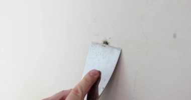 Tamirci duvardan çıkan çimentoyu spatula ile temizliyor. Kapalı çekim 4K yavaş çekim. Duvar boyama hazırlama konsepti