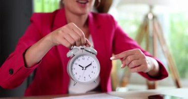 Businesswoman in pink suit pointing with index finger at alarm clock at workplace closeup 4k movie slow motion. Time management concept