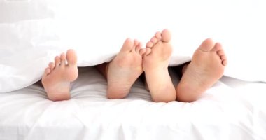 Male and female legs lying under covers in bed and stroking each other closeup 4k movie slow motion. Foreplay in sex concept