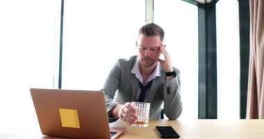 Drunk businessman drinking whiskey with glass in front of laptop at workplace 4k movie slow motion. Alcohol addiction concept