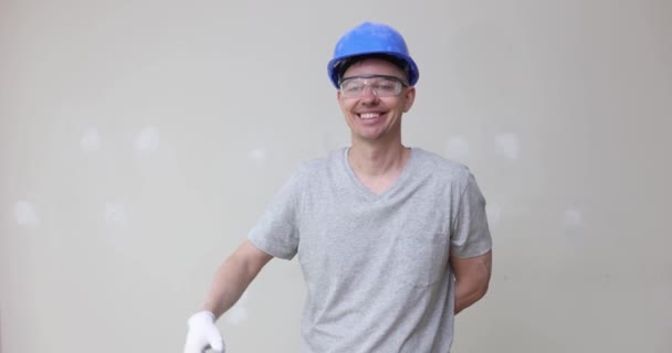 头戴头盔的男性建造者指着墙壁 涂上石膏 微笑着 电影慢动作4K 墙面抹灰质量修补工作概念 — 图库视频影像