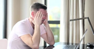 Man with headache sitting down at laptop screen at workplace 4k movie slow motion. Difficulties at work concept